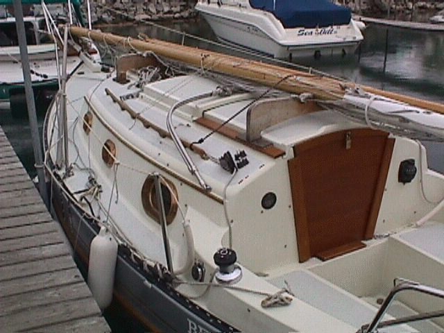 The wooden mast, gaff, and boom rest in the lazy jacks and clear the top of the bimini. The sails are already stored for the end of the season and the boat is being readied for indoor winter storage.